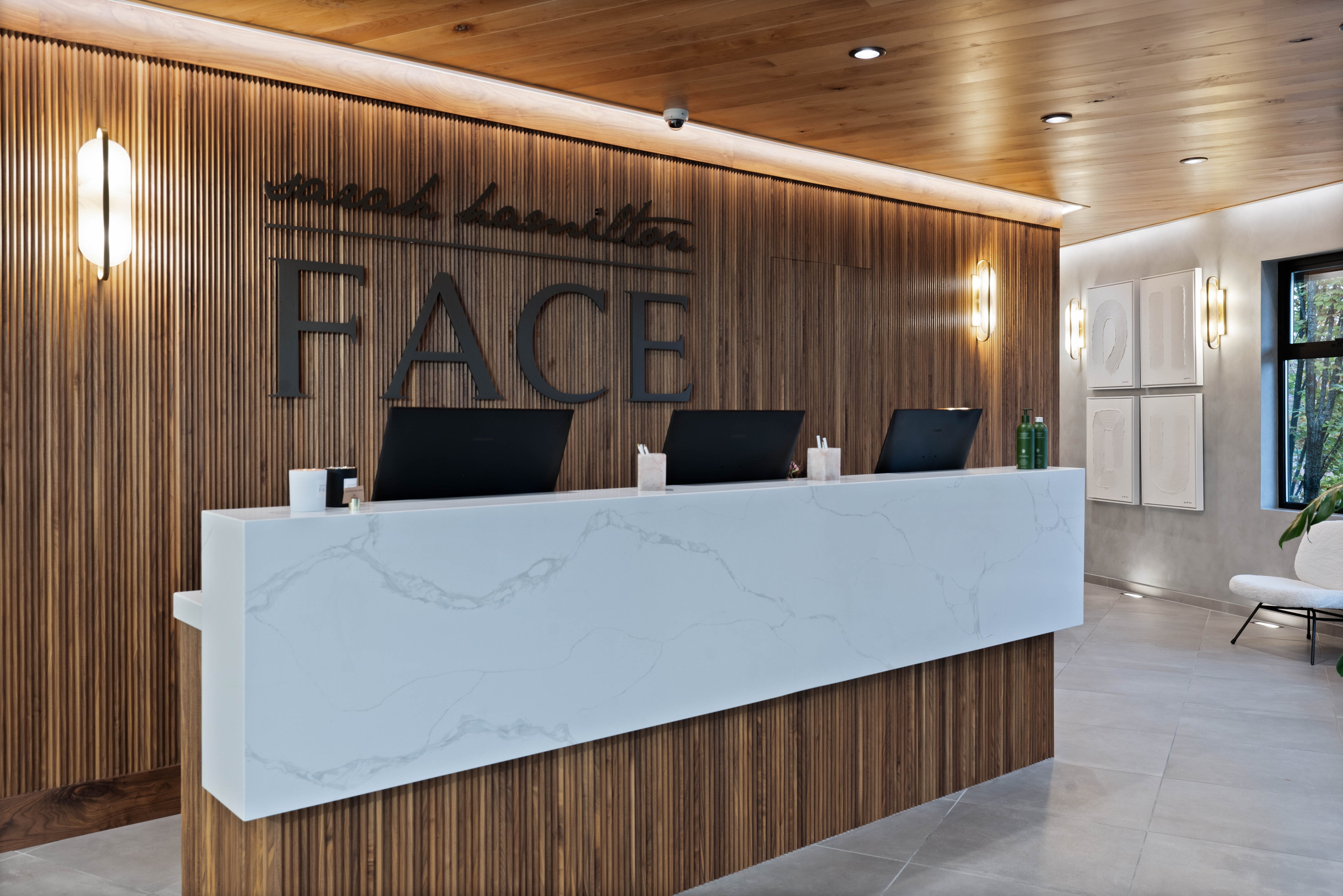 Reception area with a sleek white marble desk, wood paneling, logo on back wall, and subtle lighting, creating a warm and welcoming atmosphere.