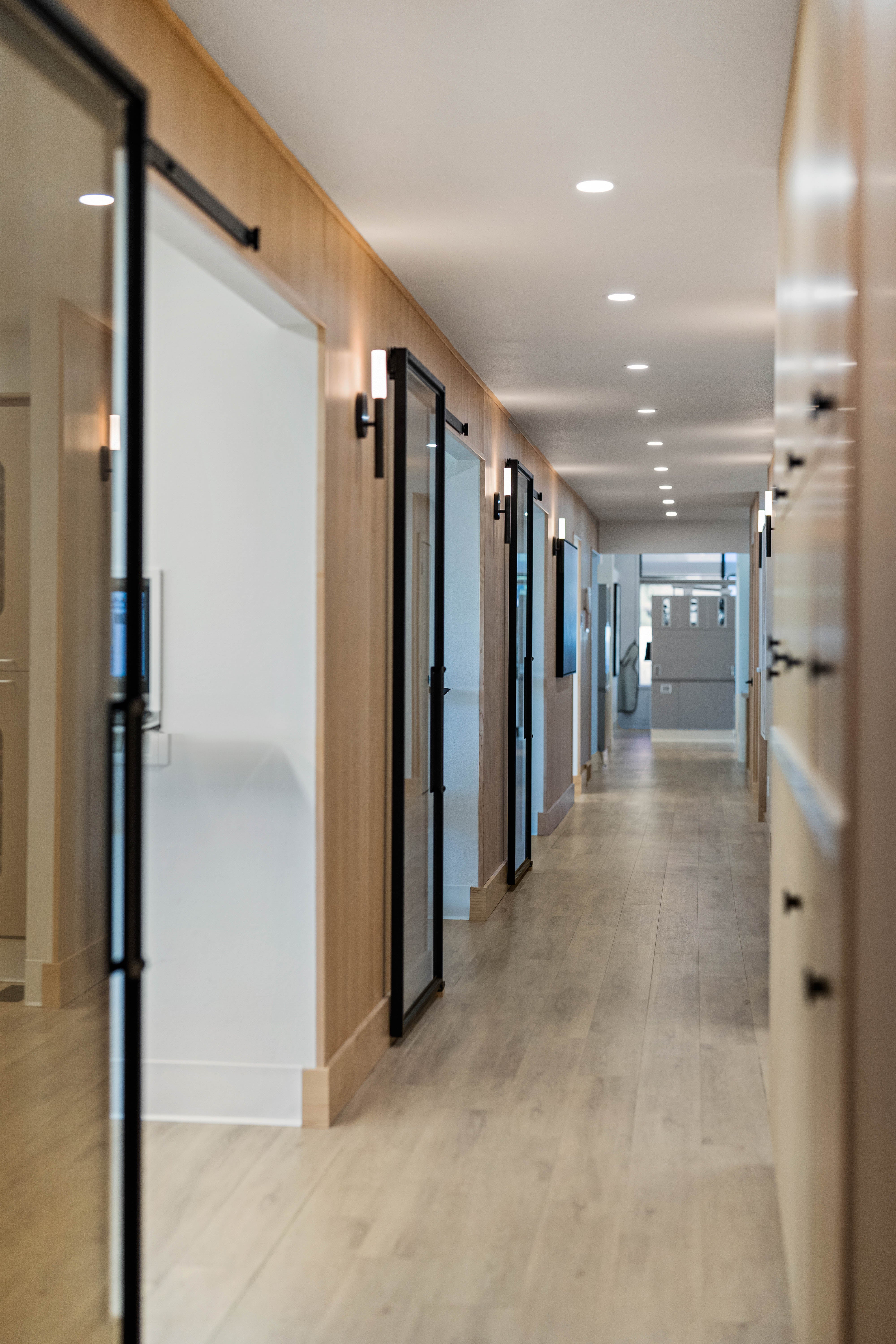 Bright hallway with fluted light wood walls, sliding glass doors, and sleek lighting, leading to private rooms.