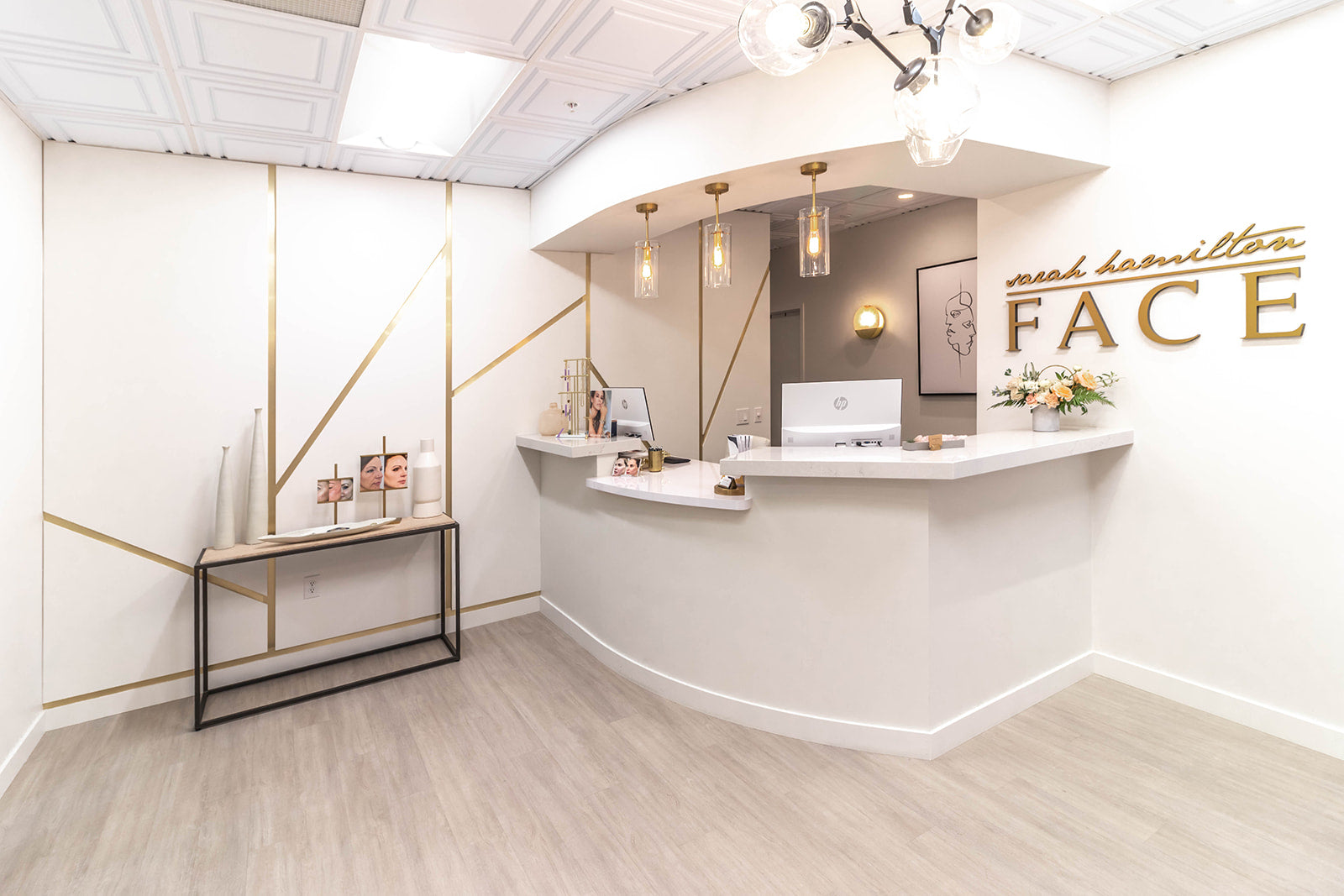 Reception area of medical spa with gold accents, modern lighting, white walls with gold brand logo next to reception desk, and white marble countertops.