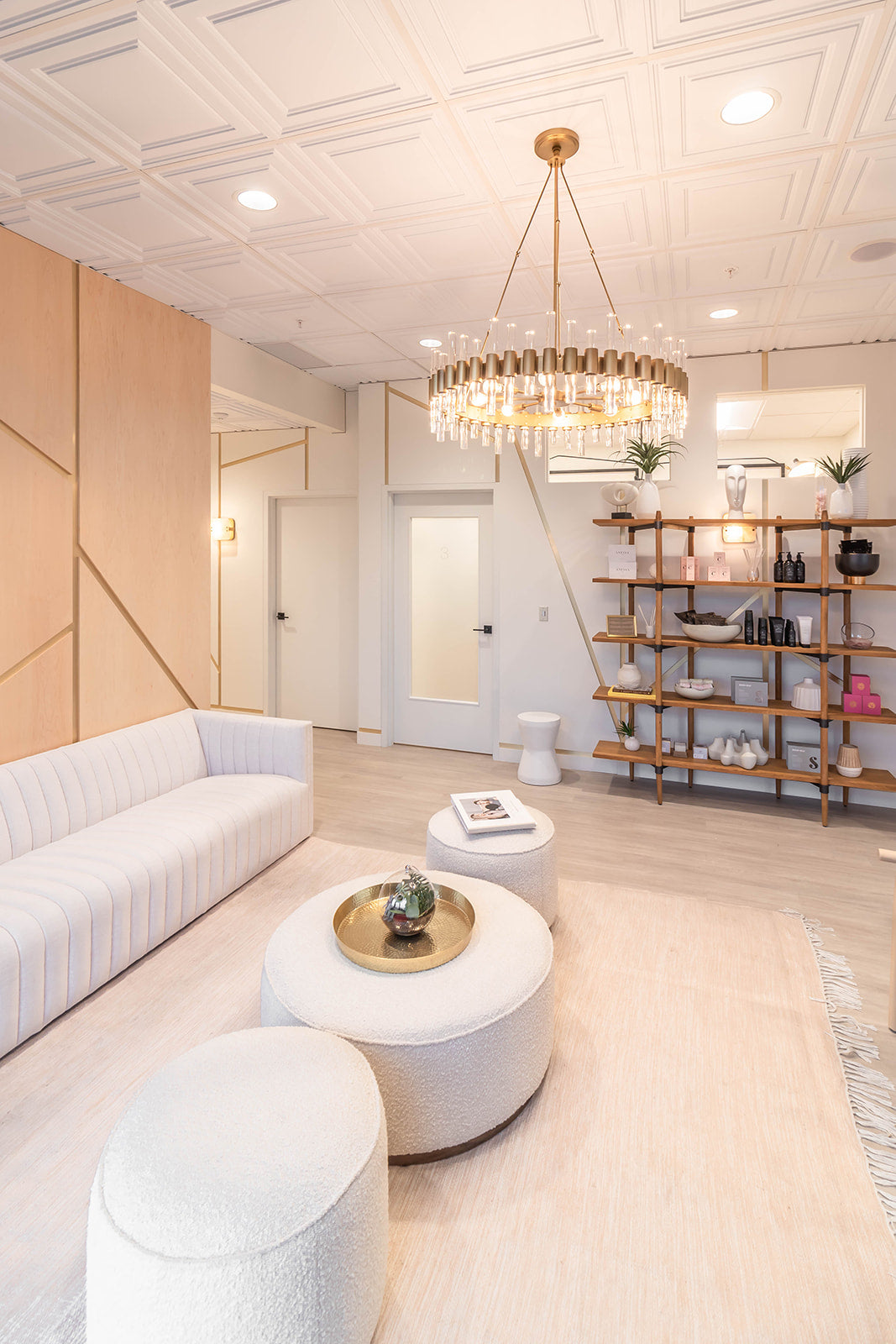 Elegant waiting area with a modern chandelier, open shelving showcasing premium skincare products, cozy seating, and stylish decor, creating a welcoming and luxurious atmosphere.