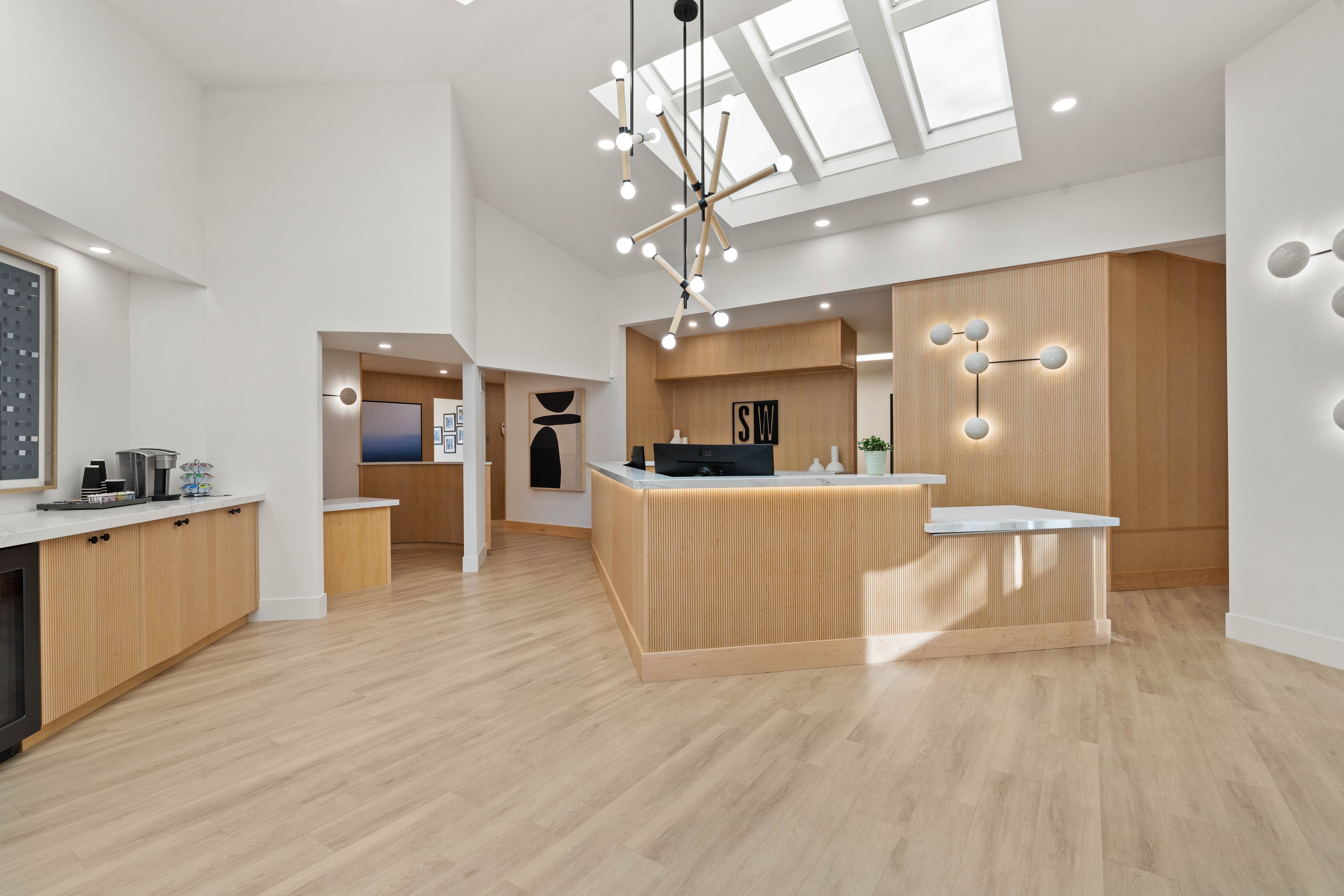 Spacious reception area with light fluted wood design, white marble countertops, skylights, modern pendant lighting, and a coffee counter.