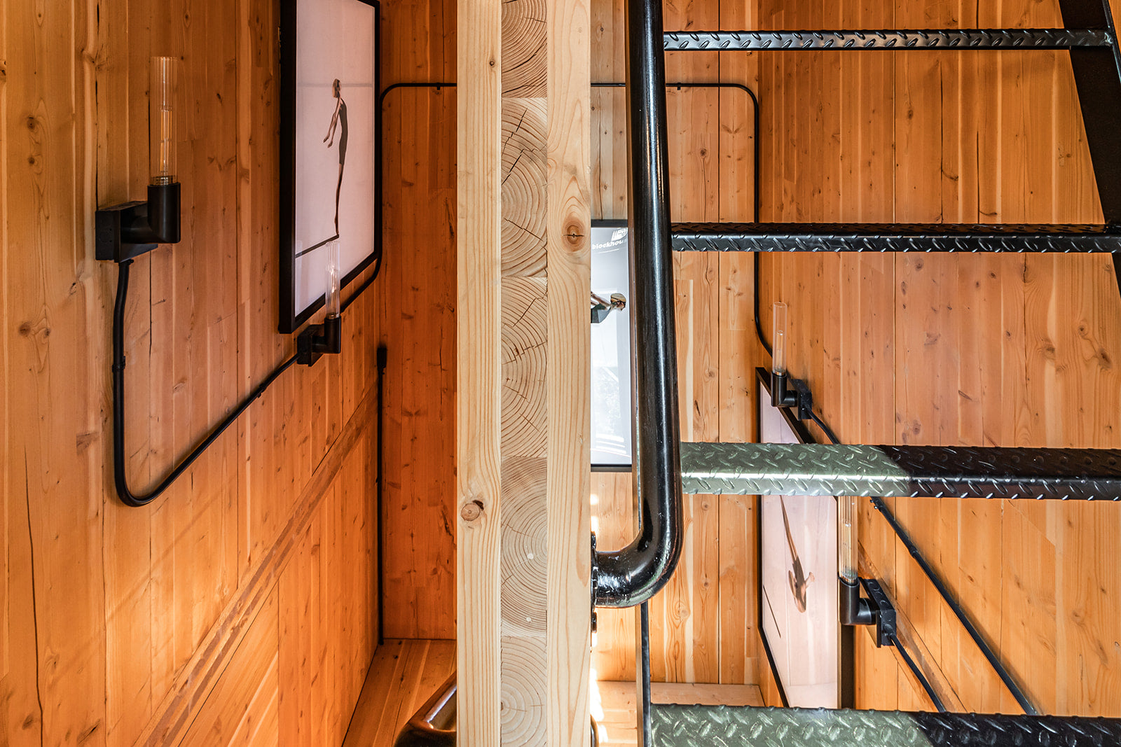 Staircase with wood paneled walls, framed photography, and black metal staircase with black railing.