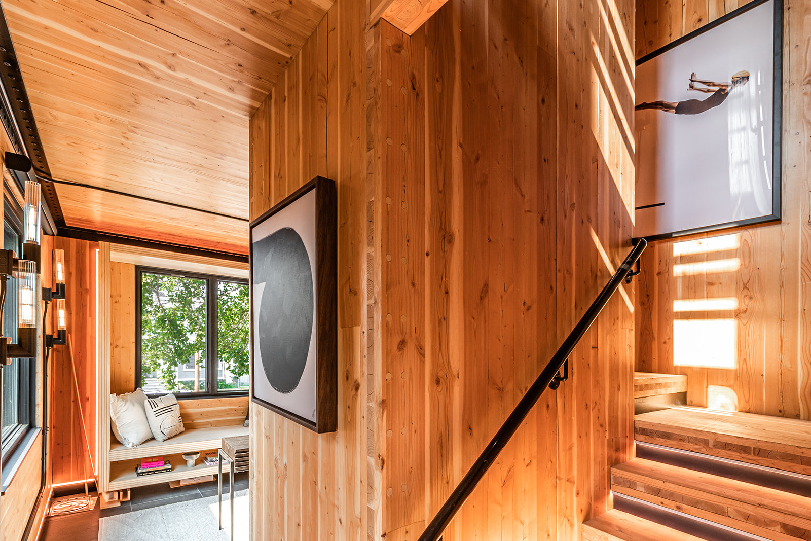 Wood-paneled interior with staircase, modern artwork, and a built-in seating nook near a large window.