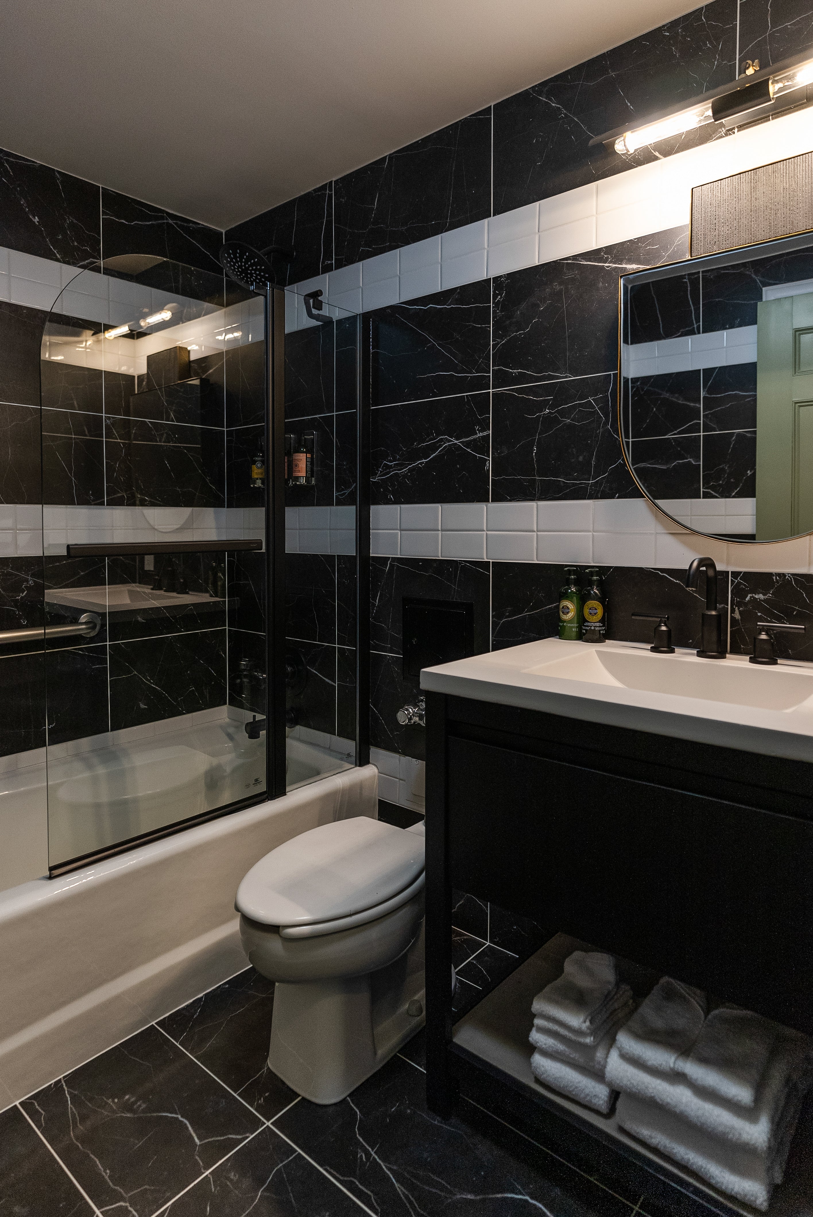 Bathroom with black marble tile, a glass-enclosed shower, white sink vanity, and sleek lighting, creating a luxurious and stylish space.