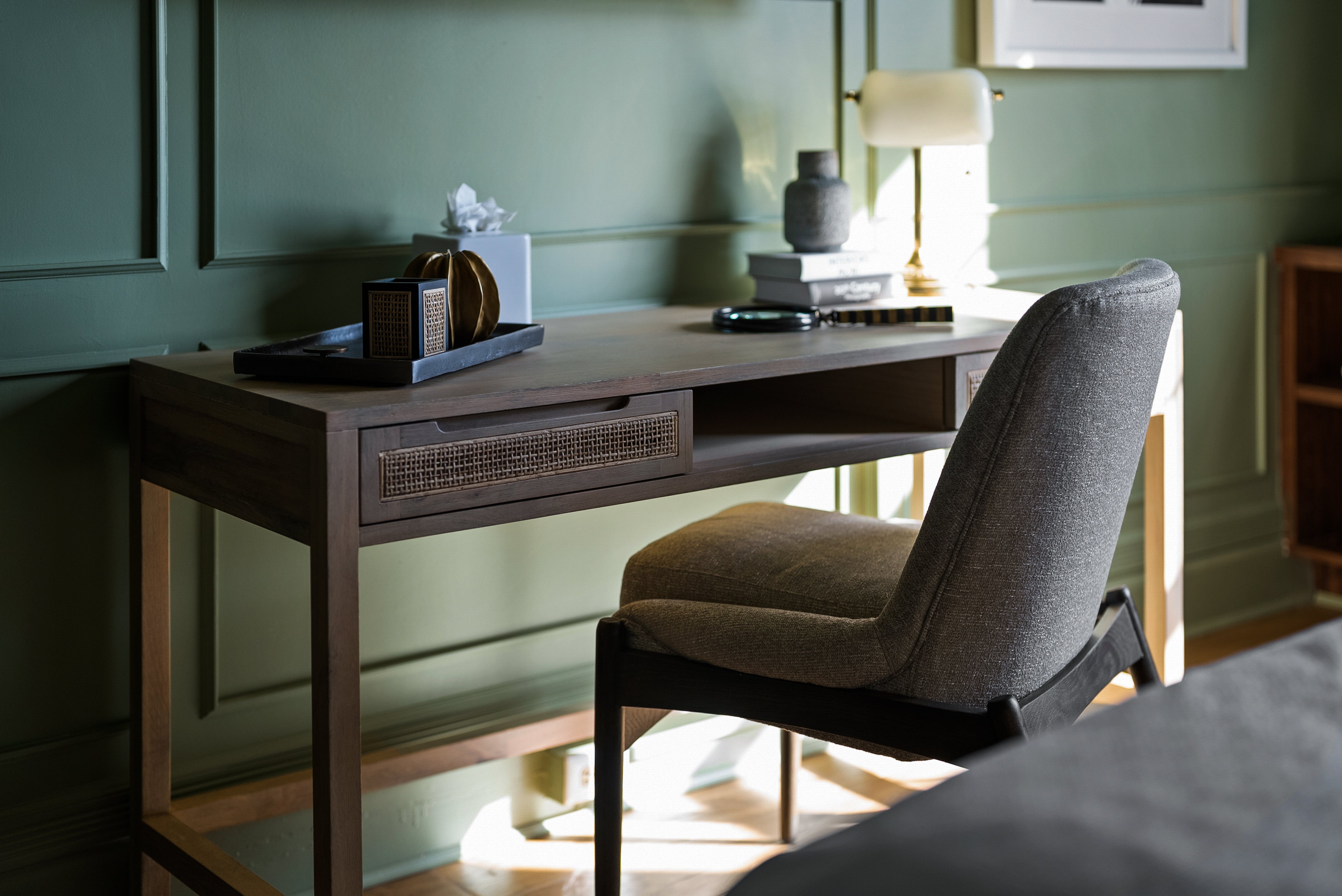 Cozy workspace with a wooden desk, gray upholstered chair, and desk decor, set against sage green walls, creating a tranquil and stylish environment.