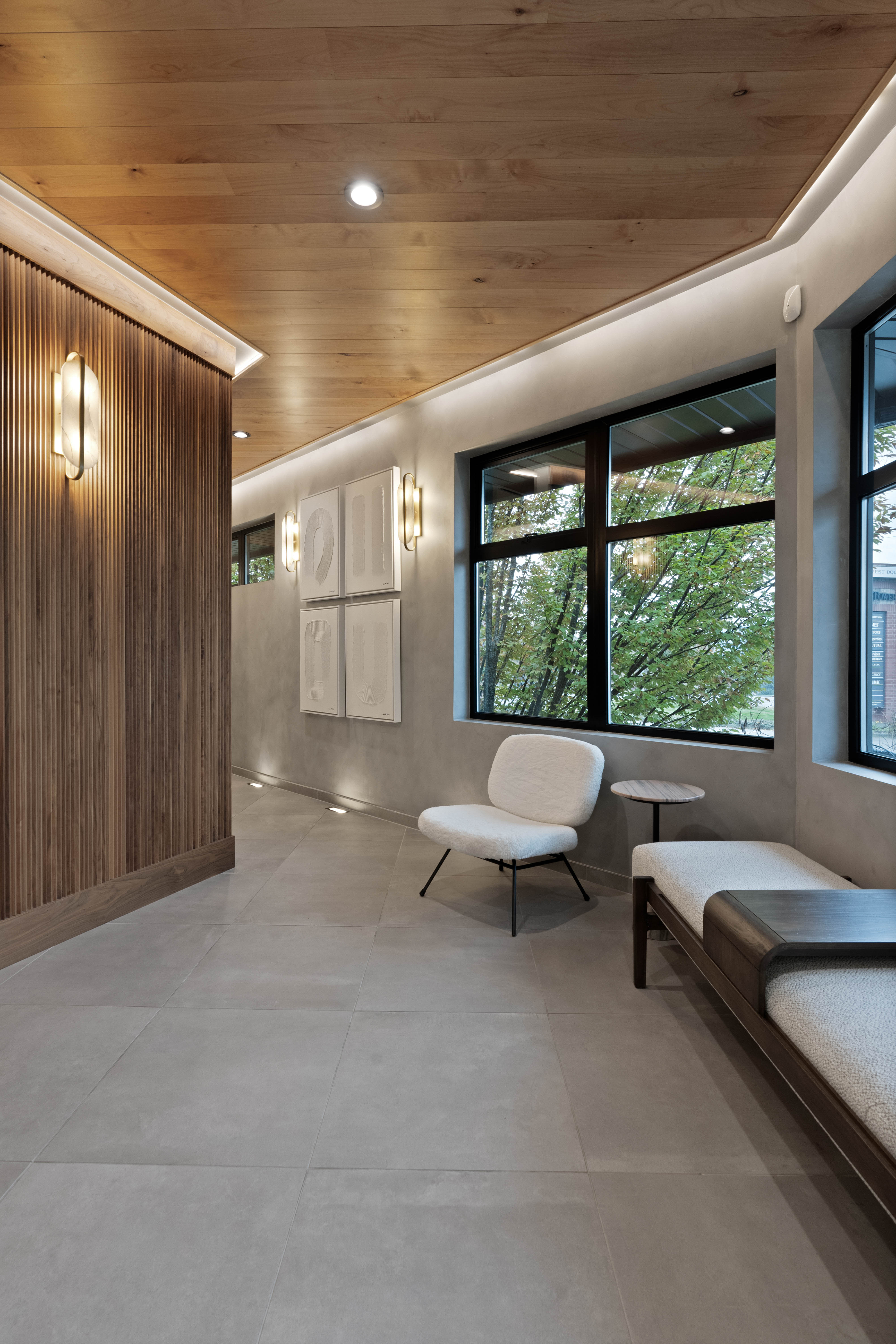 Cozy waiting area with modern seating, natural wood ceiling, and large windows overlooking lush greenery, creating a serene and inviting atmosphere.