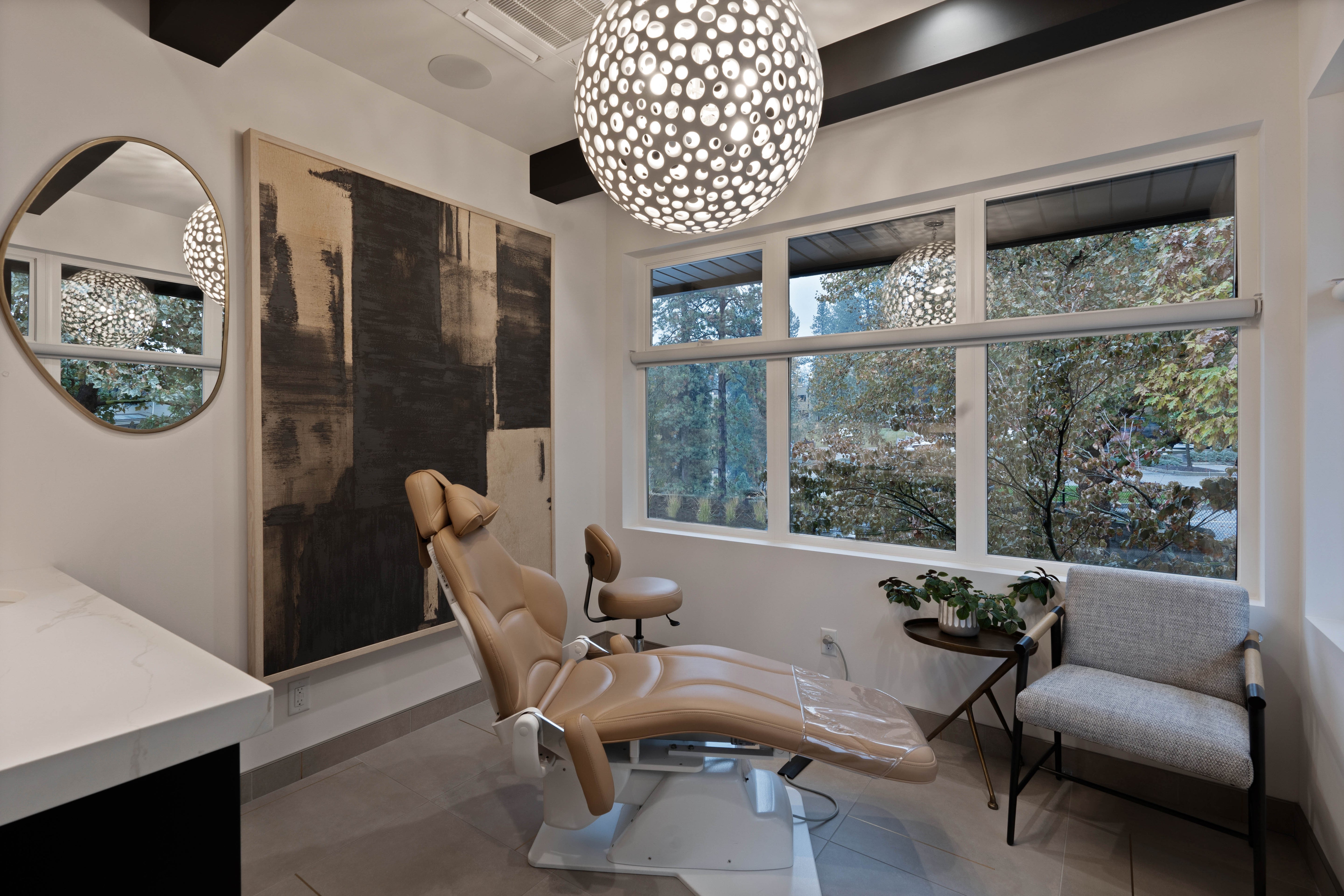 Modern treatment space with large windows, a sleek tan leather chair, and contemporary lighting fixtures.