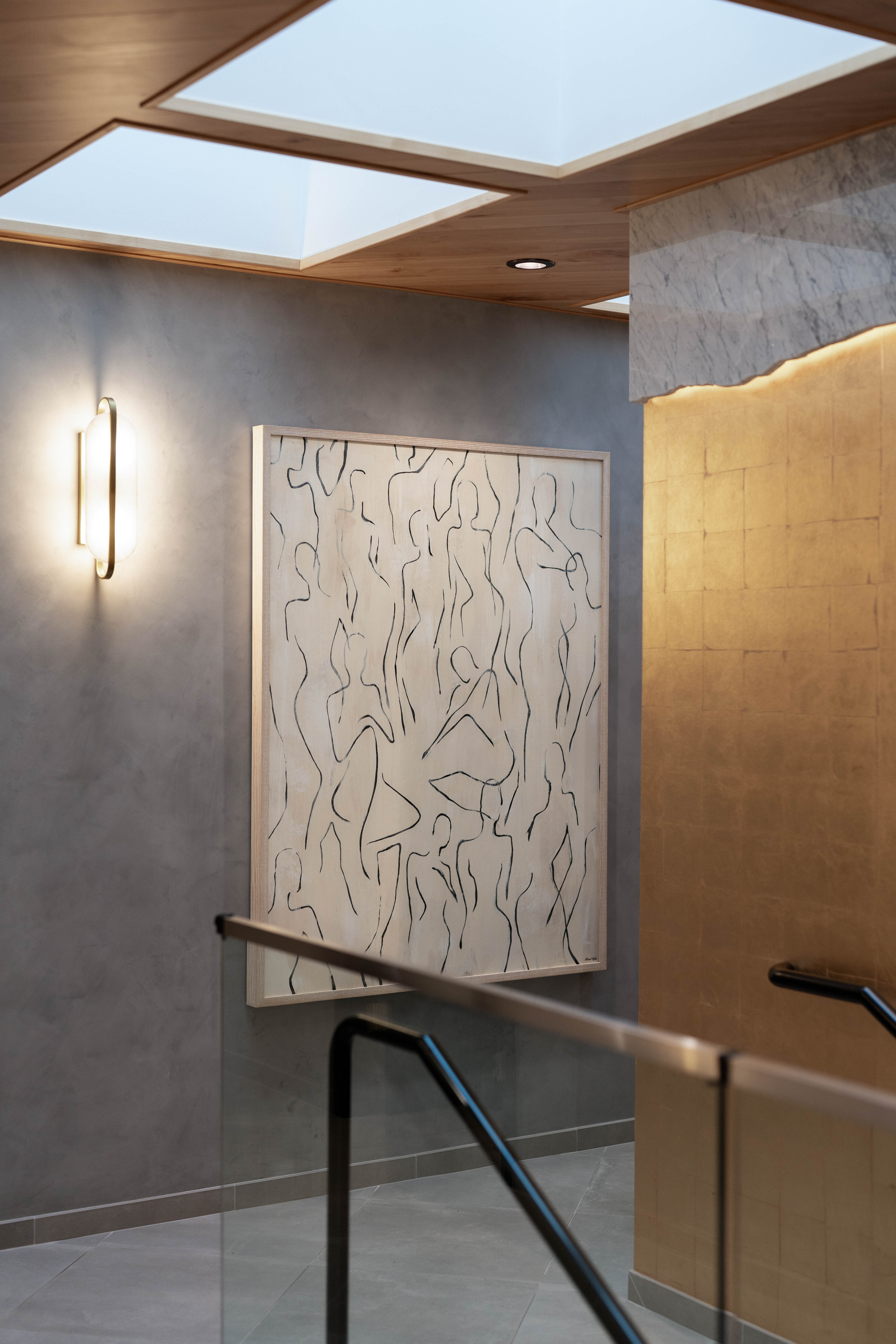 Hallway featuring a skylight, wall art with abstract human figures, gold accent wall with marble at the top, and sleek lighting, creating an elegant and artistic atmosphere.