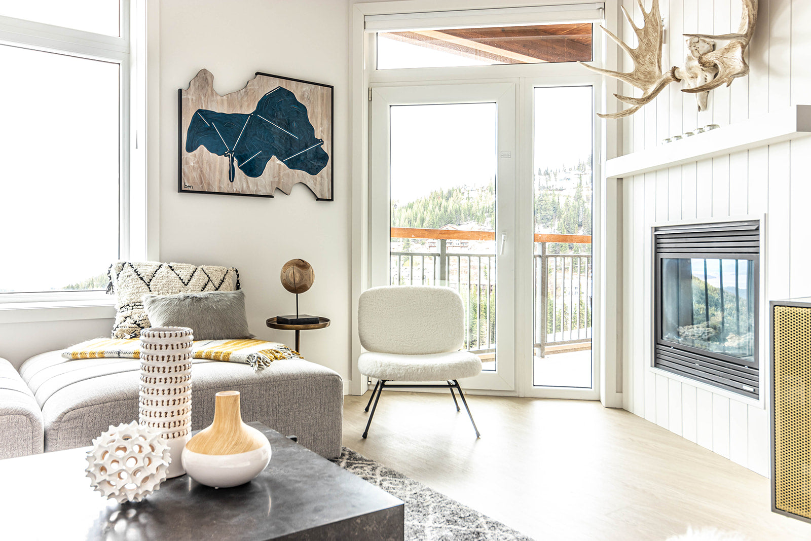 Bright living room with a cozy seating area, modern artwork, and large glass doors leading to a balcony with scenic views, complemented by a fireplace and decor.